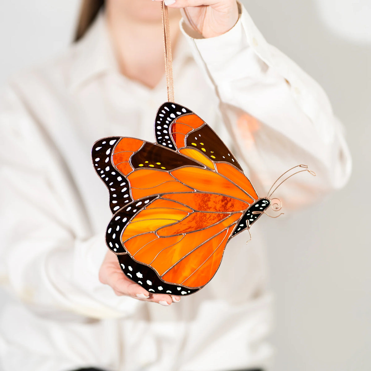 A person in a white shirt holds up a stained glass butterfly ornament with orange, yellow, black, and white details.