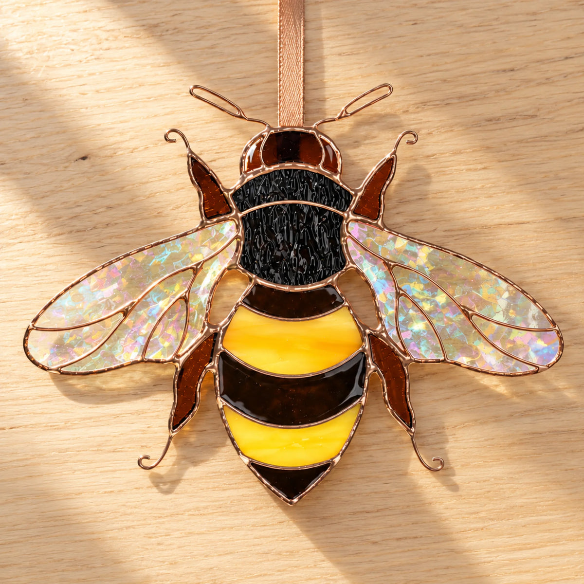 Mini bee stained glass laid flat on a light wooden table, legs and antennae shaped from copper wire