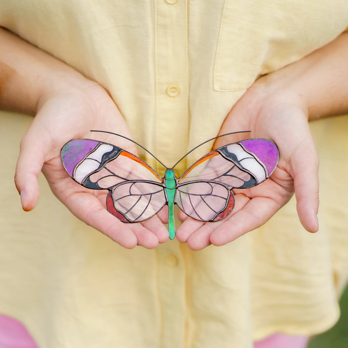 Glasswing butterfly stained glass suncatcher with purple wingtips held in open palms