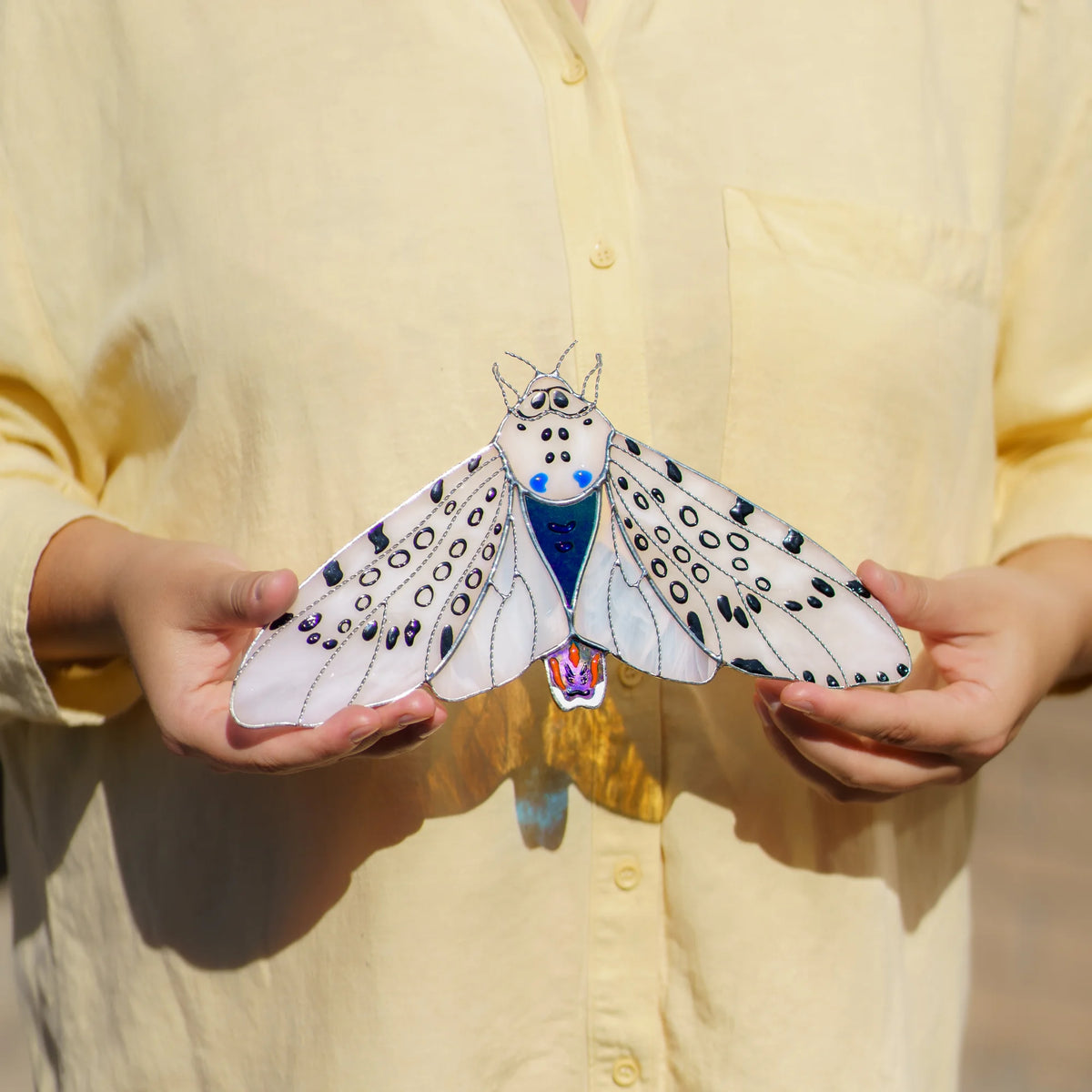 Woman holding a handmade Giant Leopard Moth stained glass window corner in both hands
