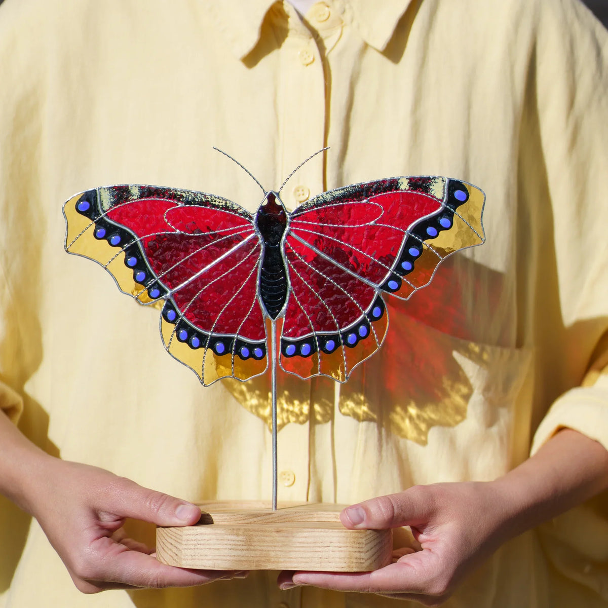 Person holding the mourning cloak butterfly stained glass suncatcher by its engraved wooden base