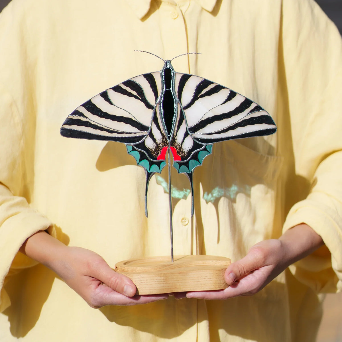 Person holding the zebra swallowtail stained glass suncatcher by its engraved wooden base