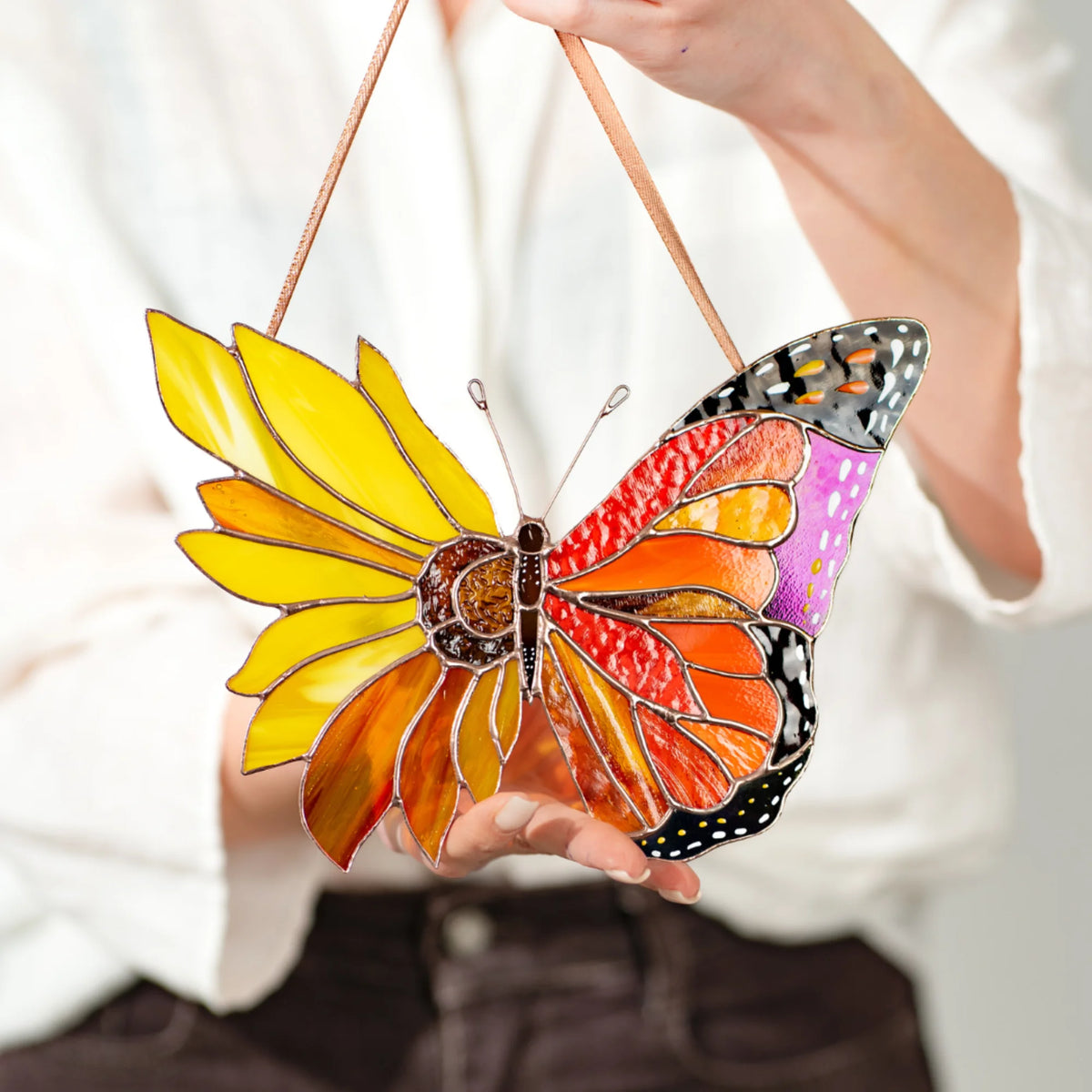 A person holding a handcrafted stained glass butterfly with a unique sunflower design, showcasing its vibrant colors as a perfect gift.