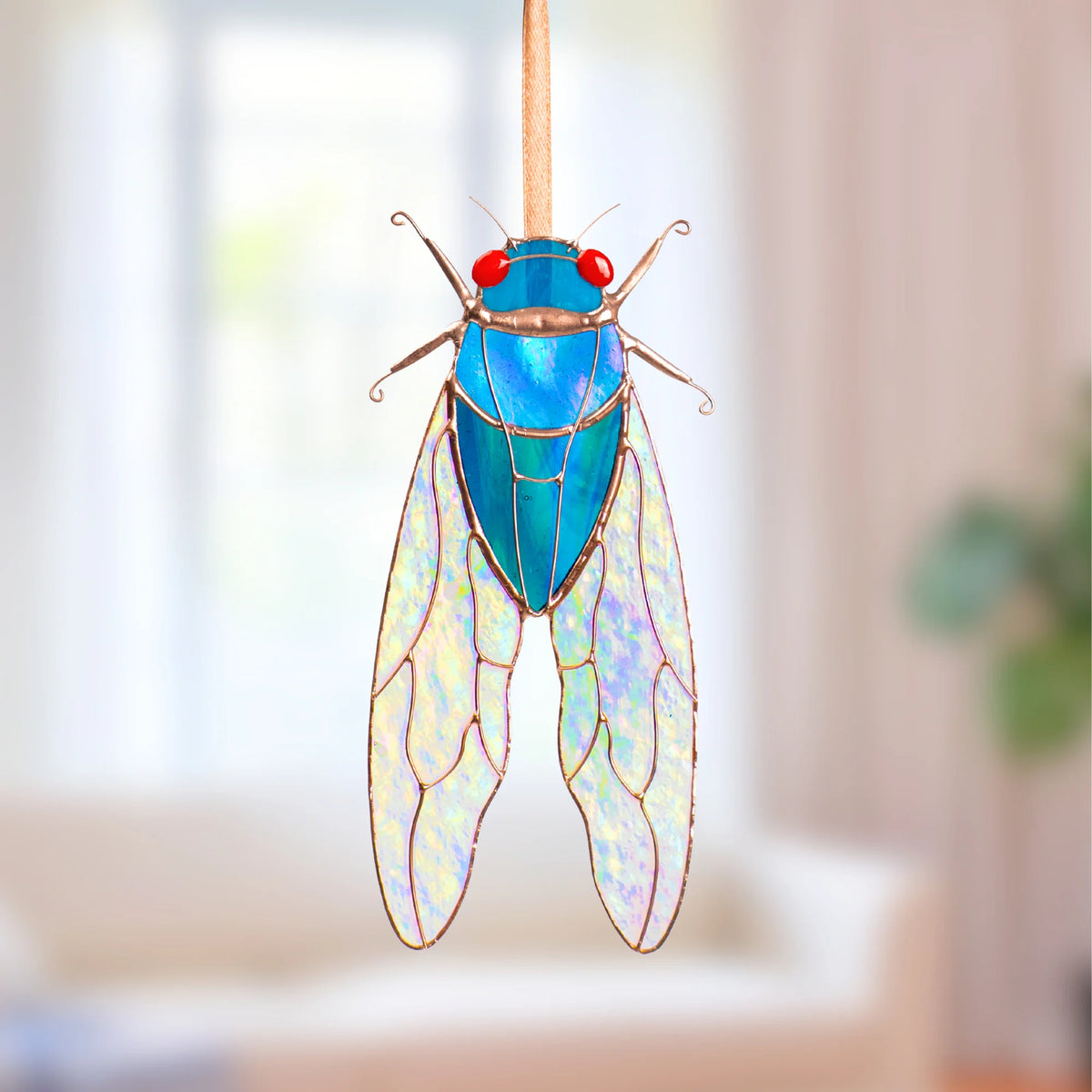 Blue stained glass cicada suncatcher variation with red glass eyes and iridescent stained glass wings, hanging on a ribbon as window decor