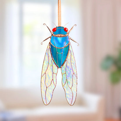 Blue stained glass cicada suncatcher variation with red glass eyes and iridescent stained glass wings, hanging on a ribbon as window decor