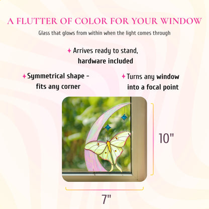 Luna moth and crescent moon stained glass window corner, 7 inches wide and 10 inches tall, shown in a window corner. Text: a flutter of color for your window, glass that glows from within when the light comes through. Arrives ready to stand with hardware included, its symmetrical shape fits any corner and turns any window into a focal point.