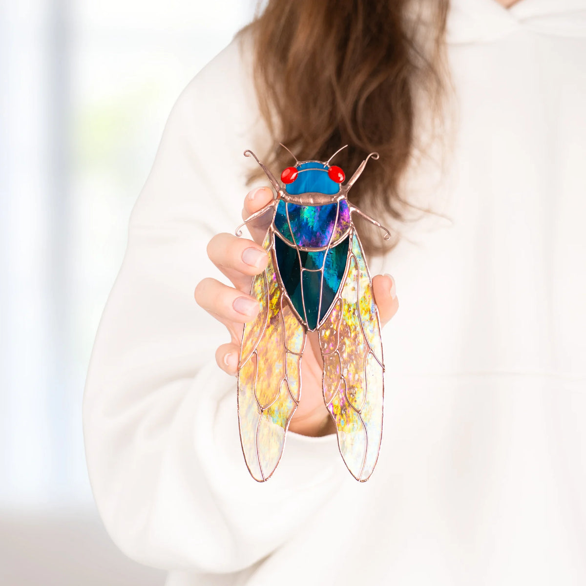 Hand holding a blue stained glass cicada variation with a violet and green iridescent glass thorax and golden stained glass wings