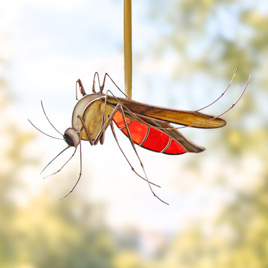 A realistic stained glass mosquito garden ornament with translucent red and brown wings, hanging from a vertical stake against a softly blurred outdoor background.