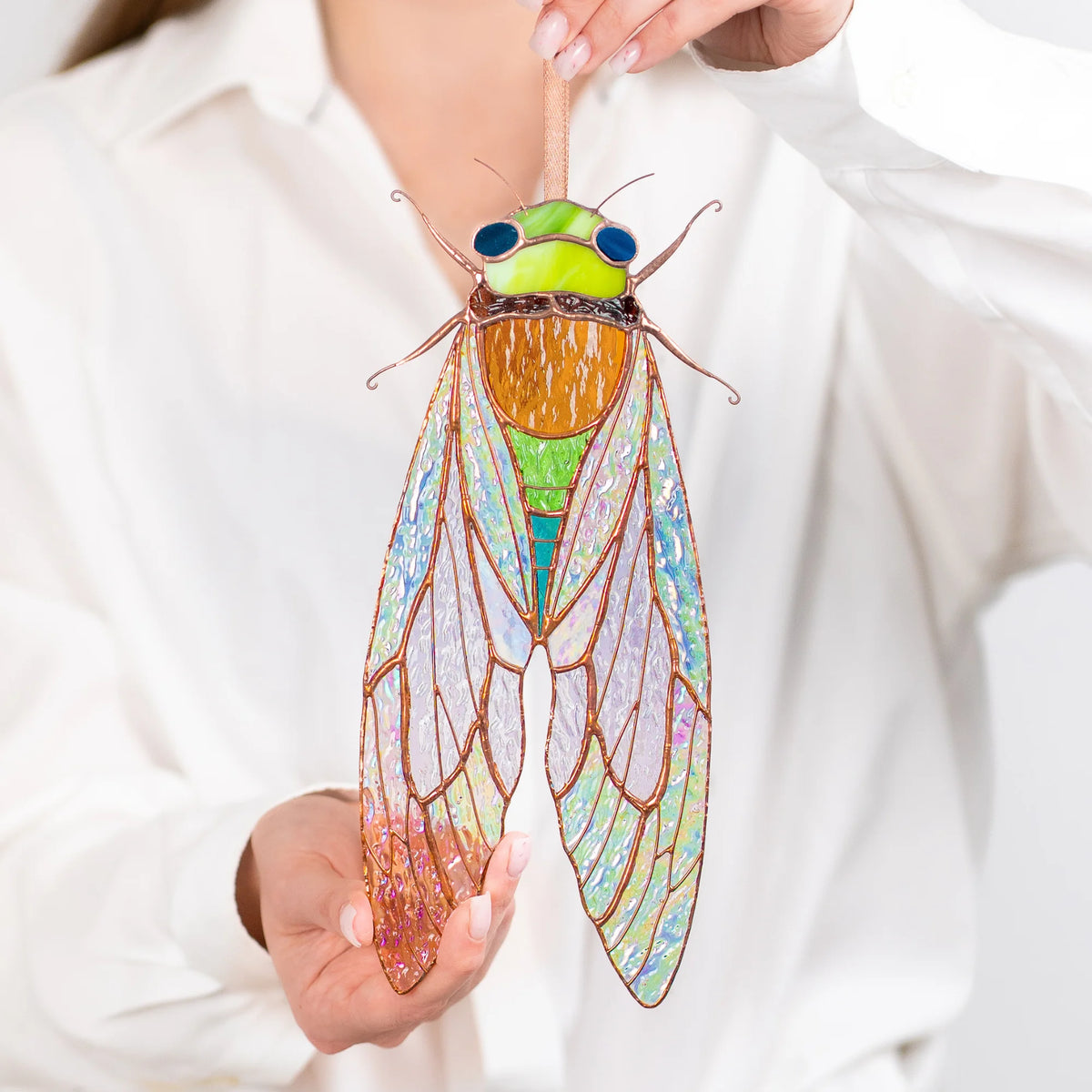 This beautiful stained glass cicada is held up against a bright background, highlighting its unique design and appeal as a special present.