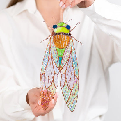 This beautiful stained glass cicada is held up against a bright background, highlighting its unique design and appeal as a special present.