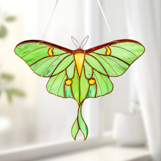 A vibrant green stained glass luna moth hanging in front of a bright window, catching the light as an exquisite decorative piece.