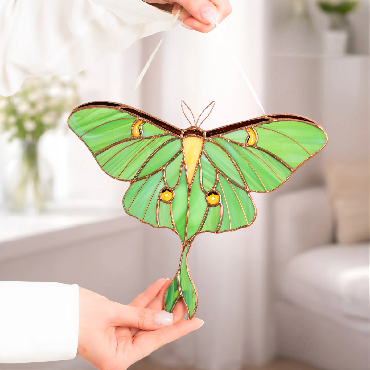 A person holding up a handcrafted green stained glass luna moth, highlighting its detailed design and beauty as a special present.