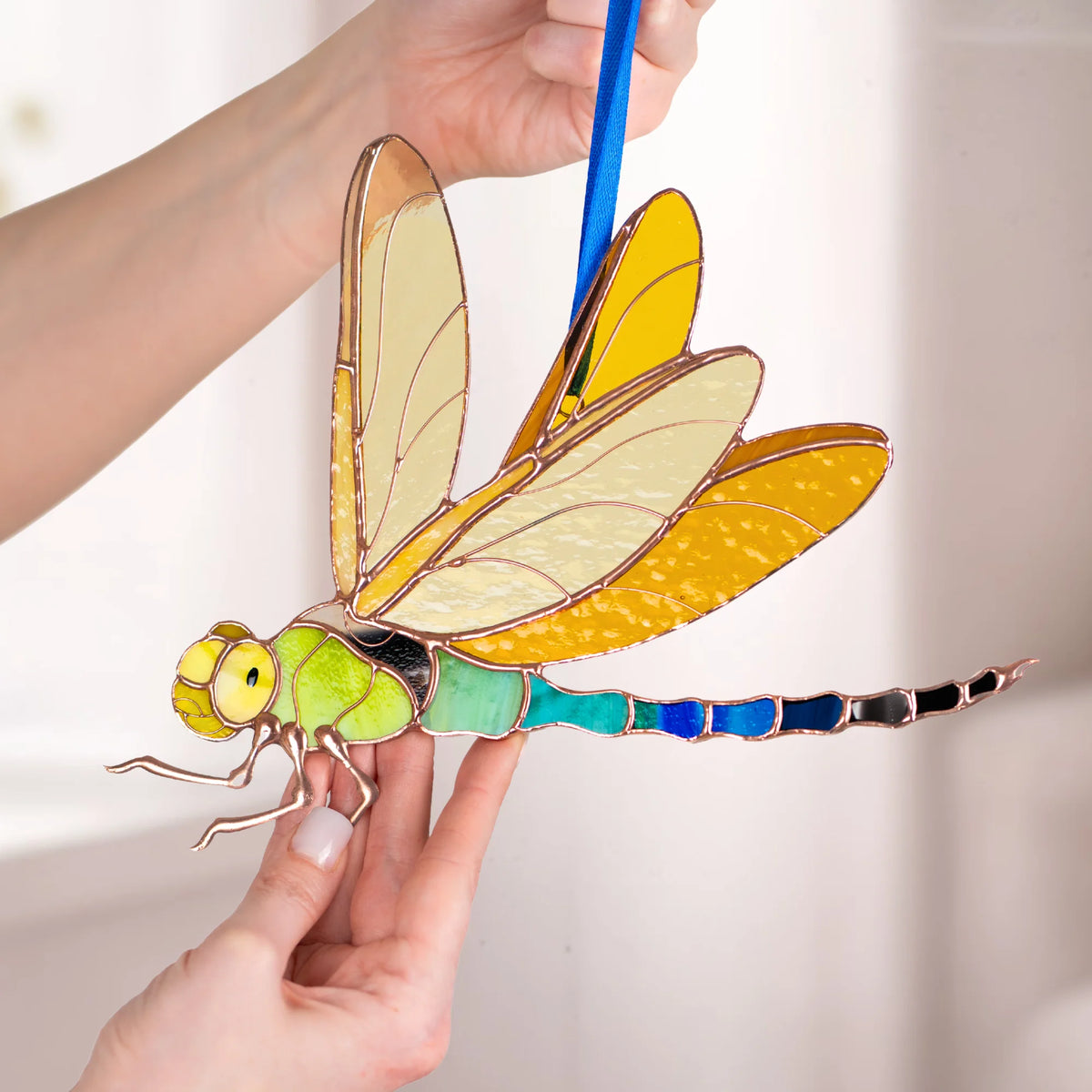 A person holding a handcrafted stained glass dragonfly, showcasing its intricate yellow and green details as a thoughtful present.