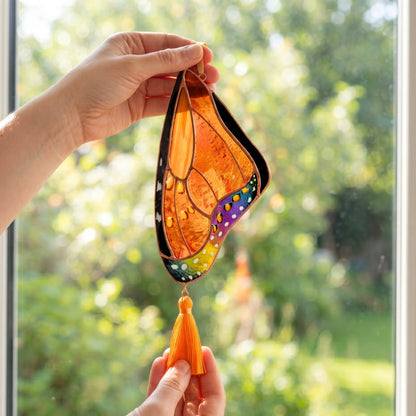 A bright stained glass monarch butterfly wing held up against a window, catching the natural light beautifully.