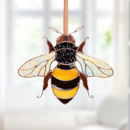 Handmade mini bee stained glass suncatcher with iridescent wings and a yellow and black striped body, hanging on a ribbon in a bright room