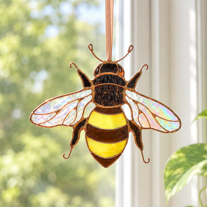 Stained glass bee hanging in a window, rainbow-sheen wings lit against a blurred garden