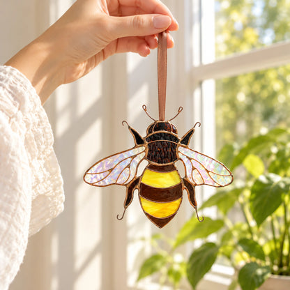 Hand hanging the bee suncatcher in a sunny window beside a green houseplant