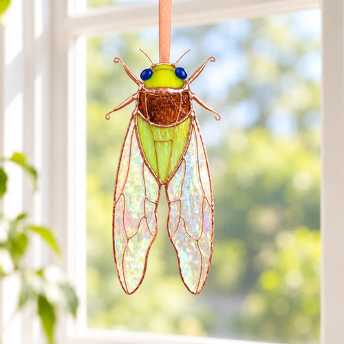 Green stained glass cicada suncatcher hanging in a sunny window, a handmade stained glass window hanging against a blurred garden
