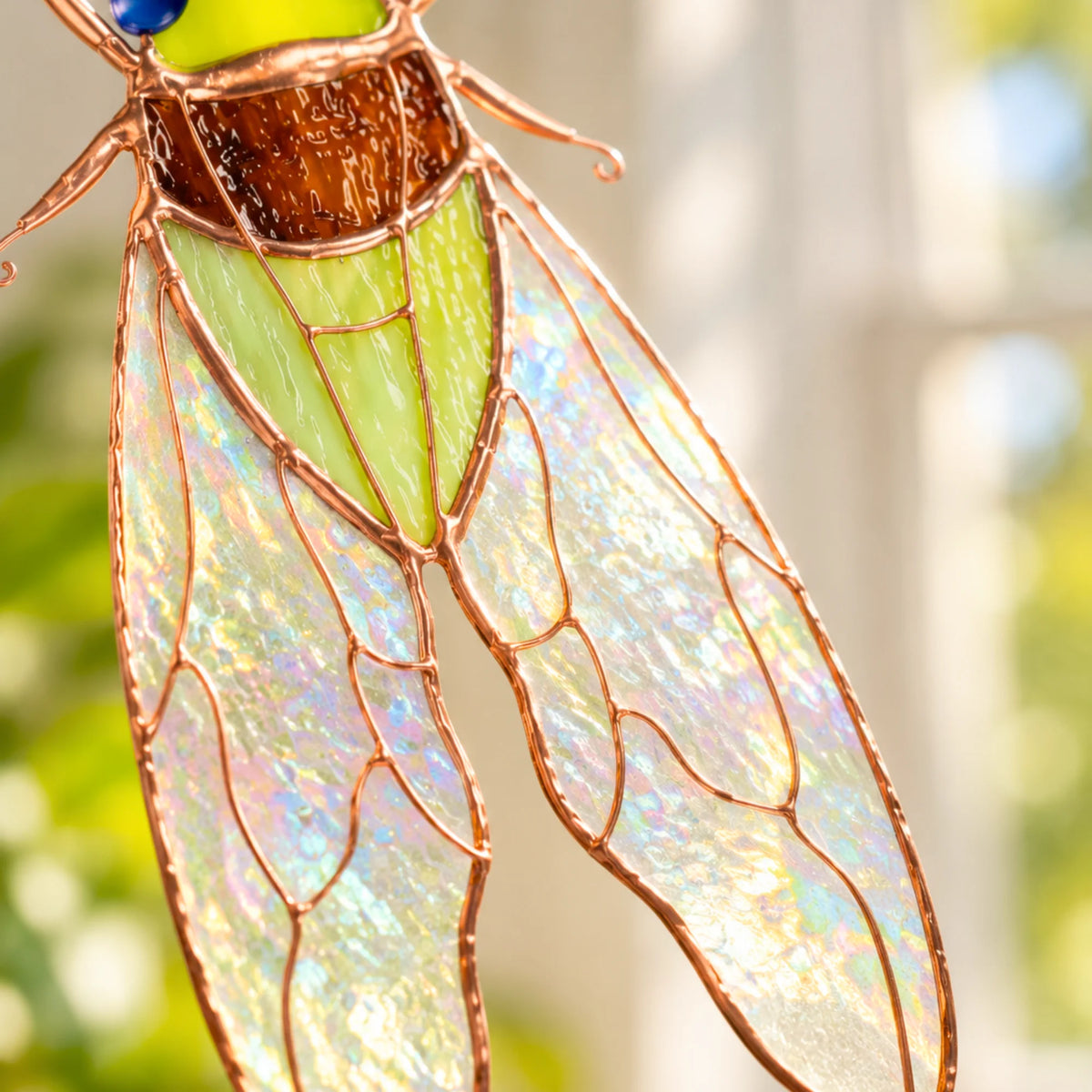 Close-up of stained glass cicada wings in clear iridescent glass with copper veins, below an amber textured stained glass thorax