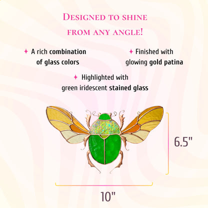 A decorative glass beetle ornament with a bright green body, gold-toned wings, and pink legs, shown on a pale pink background with size measurements of 10 inches by 6.5 inches.
