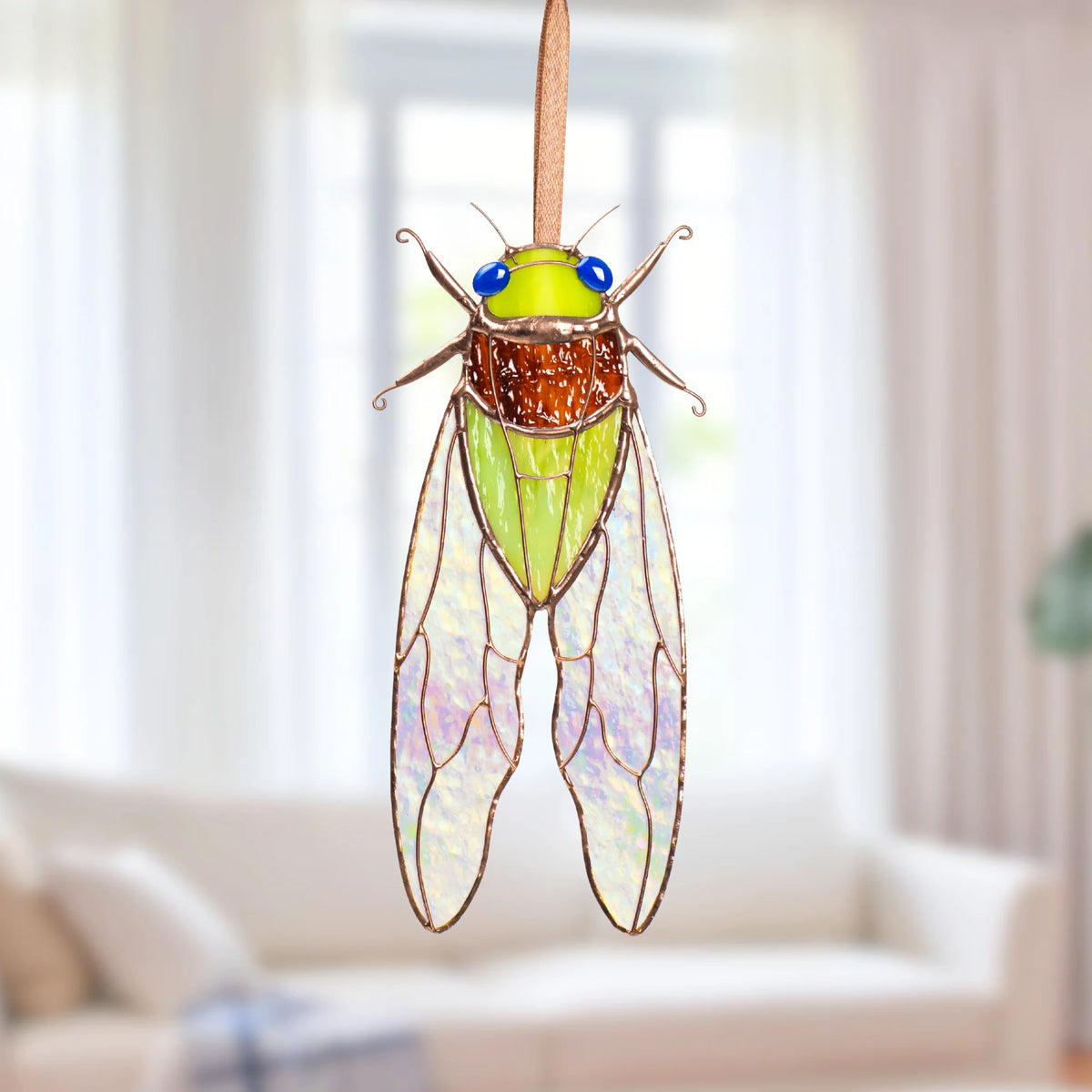 Handmade green stained glass cicada suncatcher with an amber thorax, blue glass eyes and iridescent stained glass cicada wings, hanging on a ribbon as window decor
