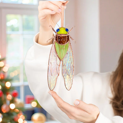Woman holding a stained glass cicada suncatcher by its ribbon beside a Christmas tree, a handmade stained glass insect ornament and gift idea