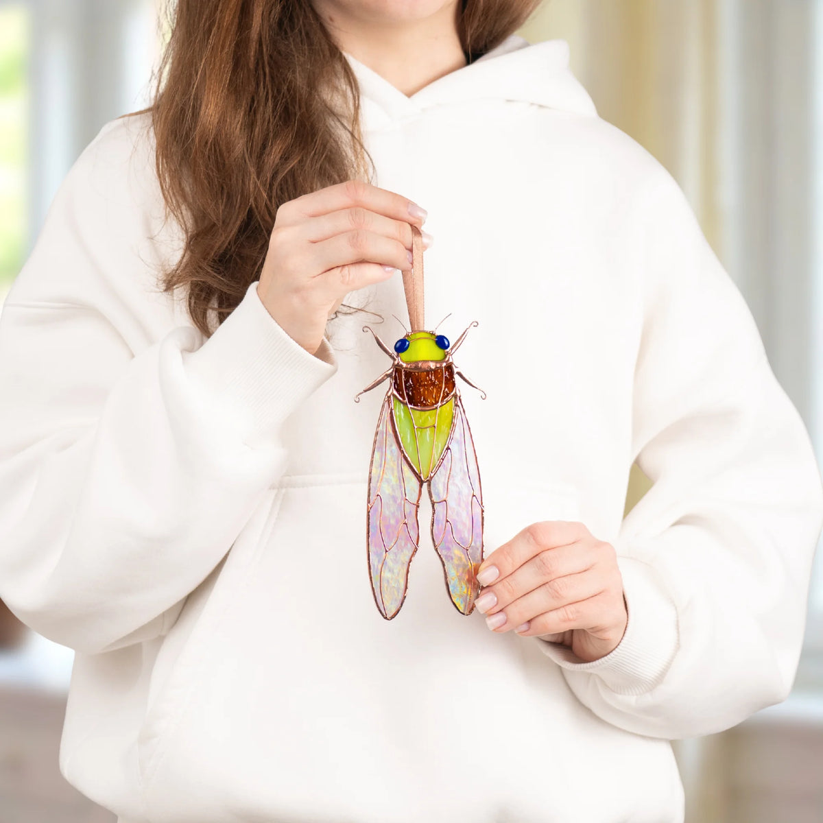 Woman in a white hoodie holding a green stained glass cicada suncatcher to show its size, handmade stained glass insect art