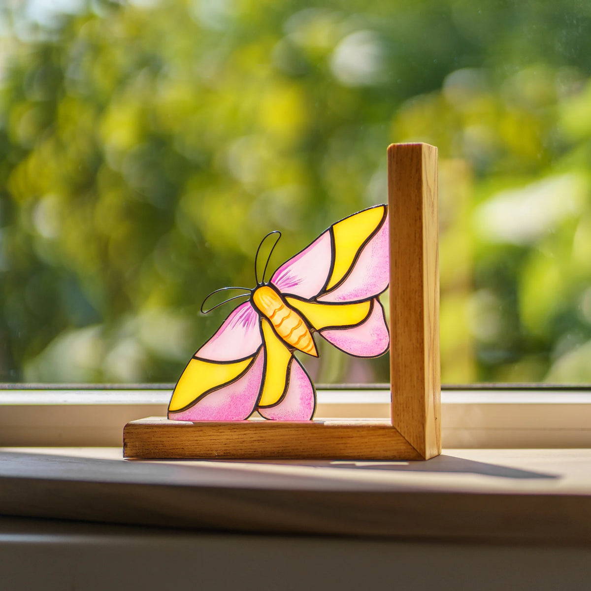 This handcrafted pink and yellow stained glass moth bookend catches the natural light, serving as a delightful and unique decor piece.