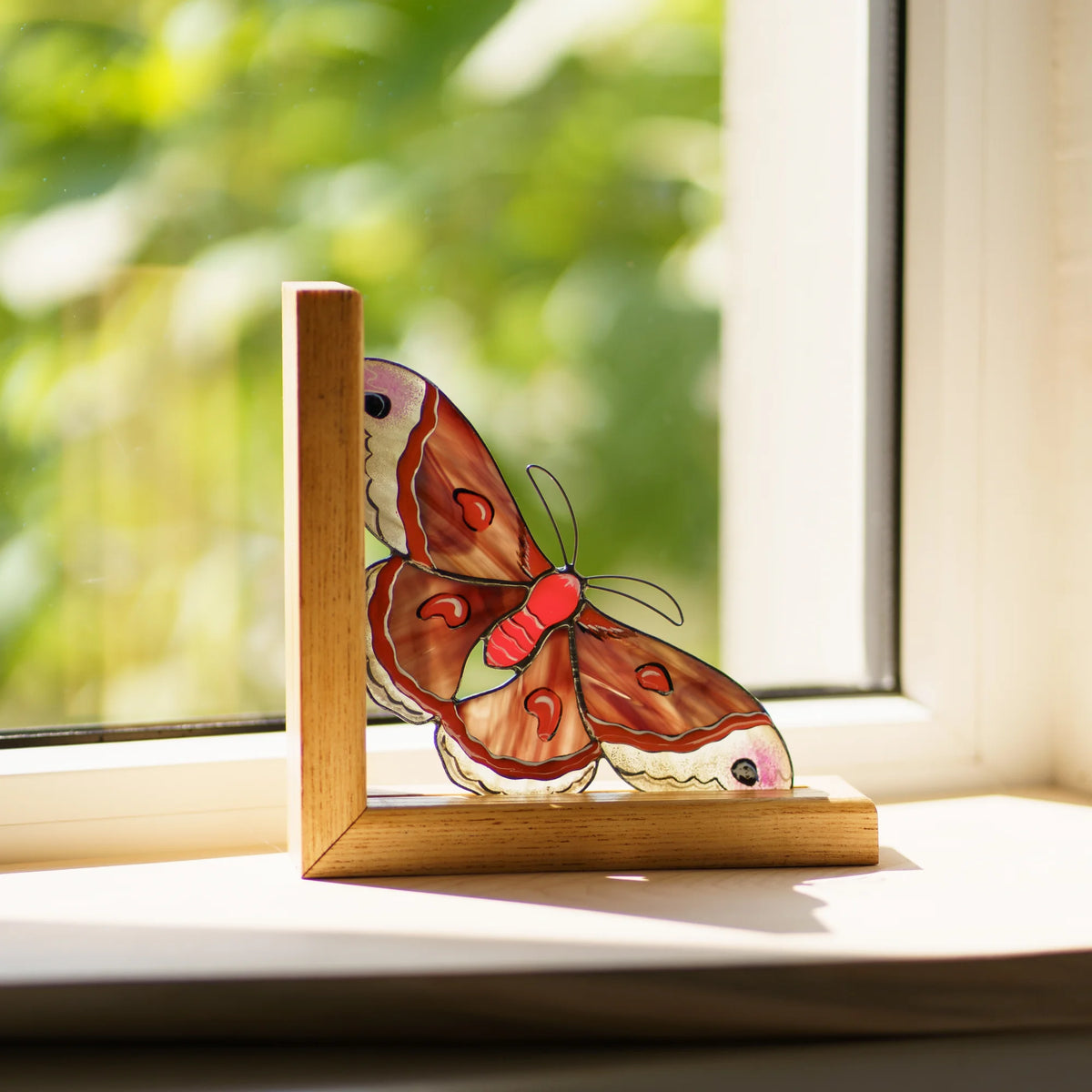 This handcrafted red stained glass moth bookend catches the natural light, serving as a delightful and unique decor piece.