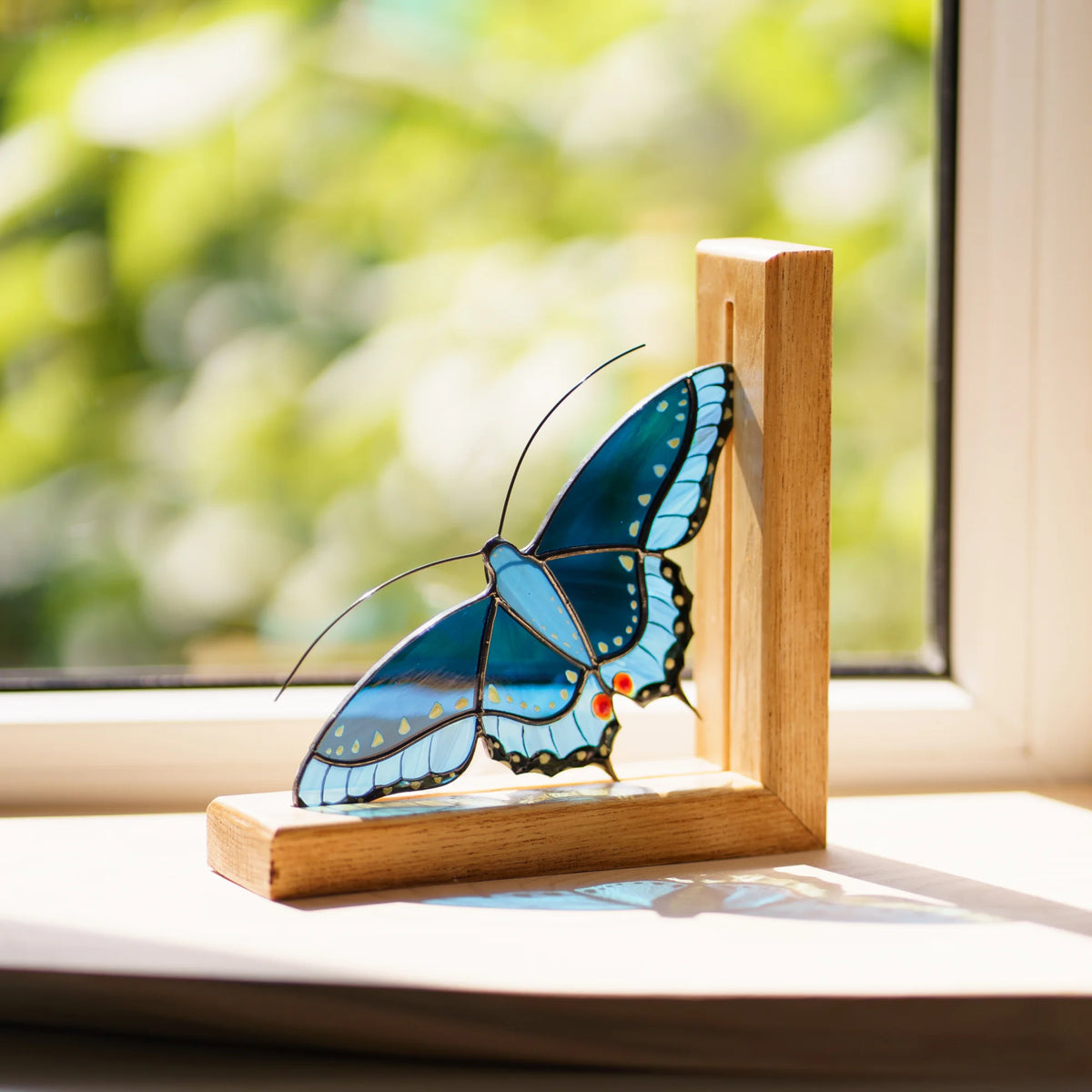 This stunning blue stained glass butterfly bookend is the perfect addition to a sunny windowsill, creating a beautiful play of light and shadow.