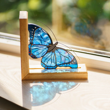 A stunning blue stained glass butterfly bookend capturing the warm sunlight on a windowsill, casting a vibrant blue shadow and adding an artistic touch to any room.