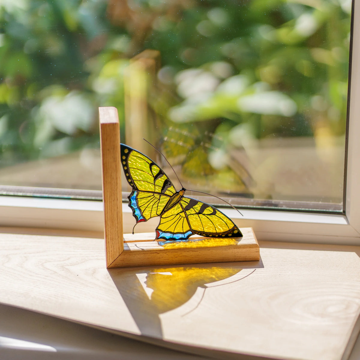 A stunning yellow stained glass butterfly bookend placed on a wooden windowsill, making a wonderful gift for book lovers.