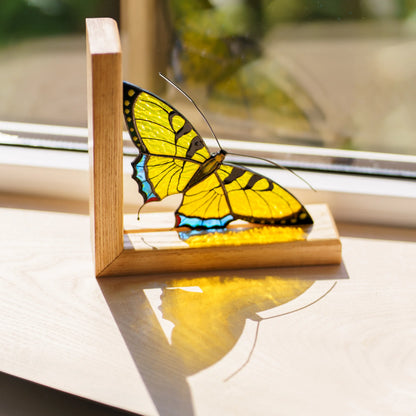 This handcrafted yellow stained glass butterfly bookend catches the sunlight on a windowsill, serving as a charming and unique decor piece.