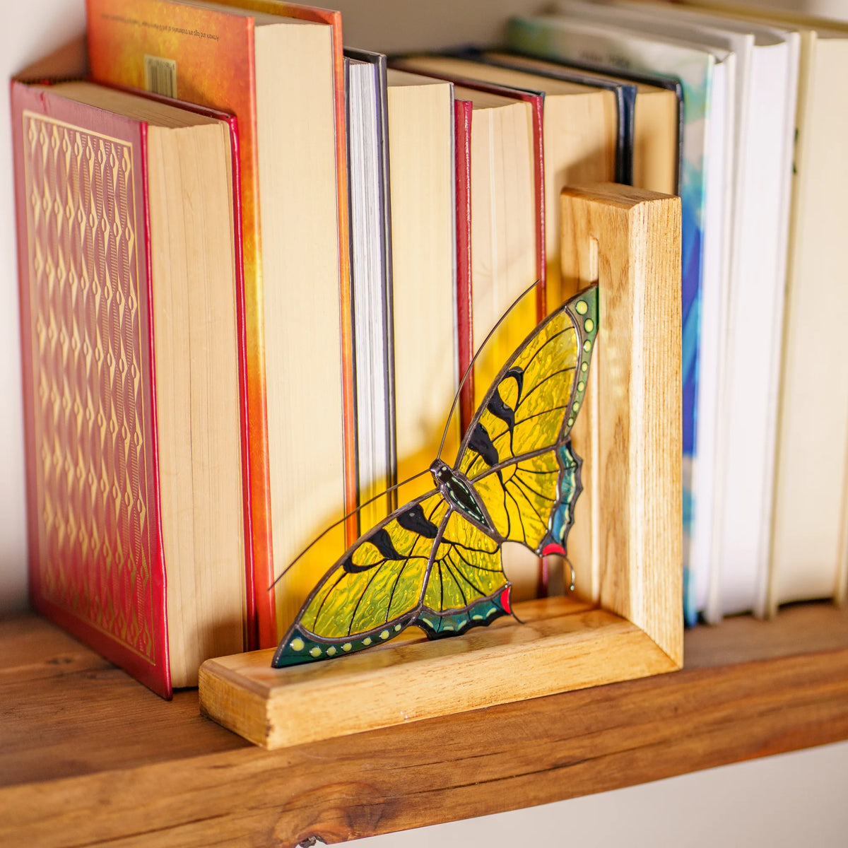 A gorgeous yellow stained glass butterfly bookend neatly holding books on a wooden shelf, making a thoughtful and practical gift.