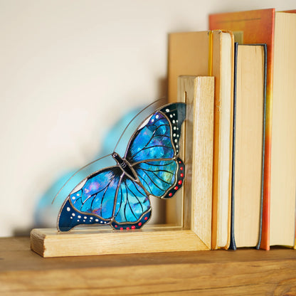 A charming blue stained glass butterfly bookend elegantly holding a row of books on a wooden shelf, offering both practical support and a sophisticated decorative accent.