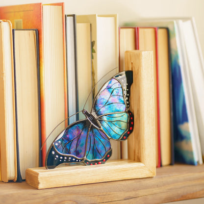 A vibrant blue stained glass butterfly bookend securely organizing books on a wooden shelf, creating a wonderful blend of functionality and artistic charm for a home library.