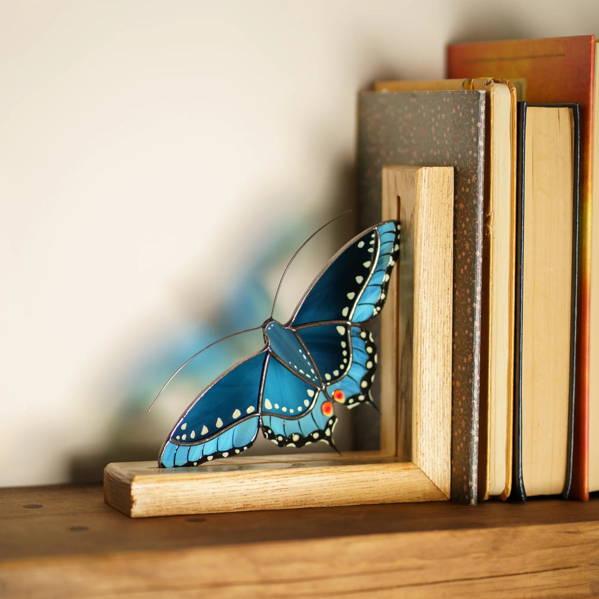 This unique blue stained glass butterfly bookend sits nestled among a row of books on a wooden shelf, adding a touch of artistry to your home library.