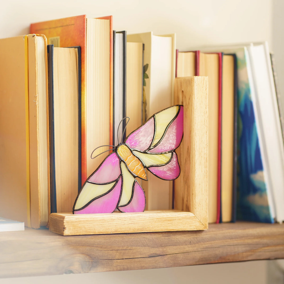 This detailed pink and yellow stained glass moth bookend holds books upright on a shelf, highlighting its appeal as a memorable home decor gift.