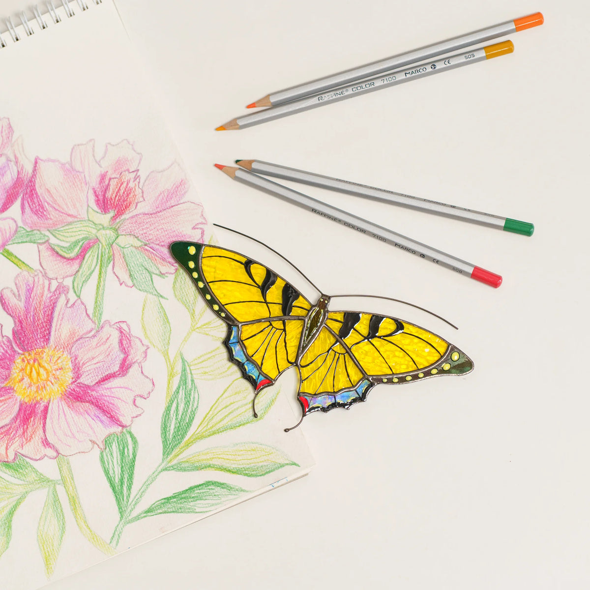 Yellow swallowtail butterfly suncatcher with black stripes and iridescent blue tail edges, on a floral sketchbook