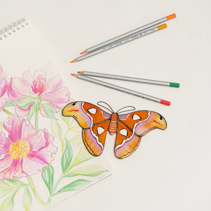 Atlas moth stained glass suncatcher in orange and lilac glass with snake-head wingtips, on a peony sketch