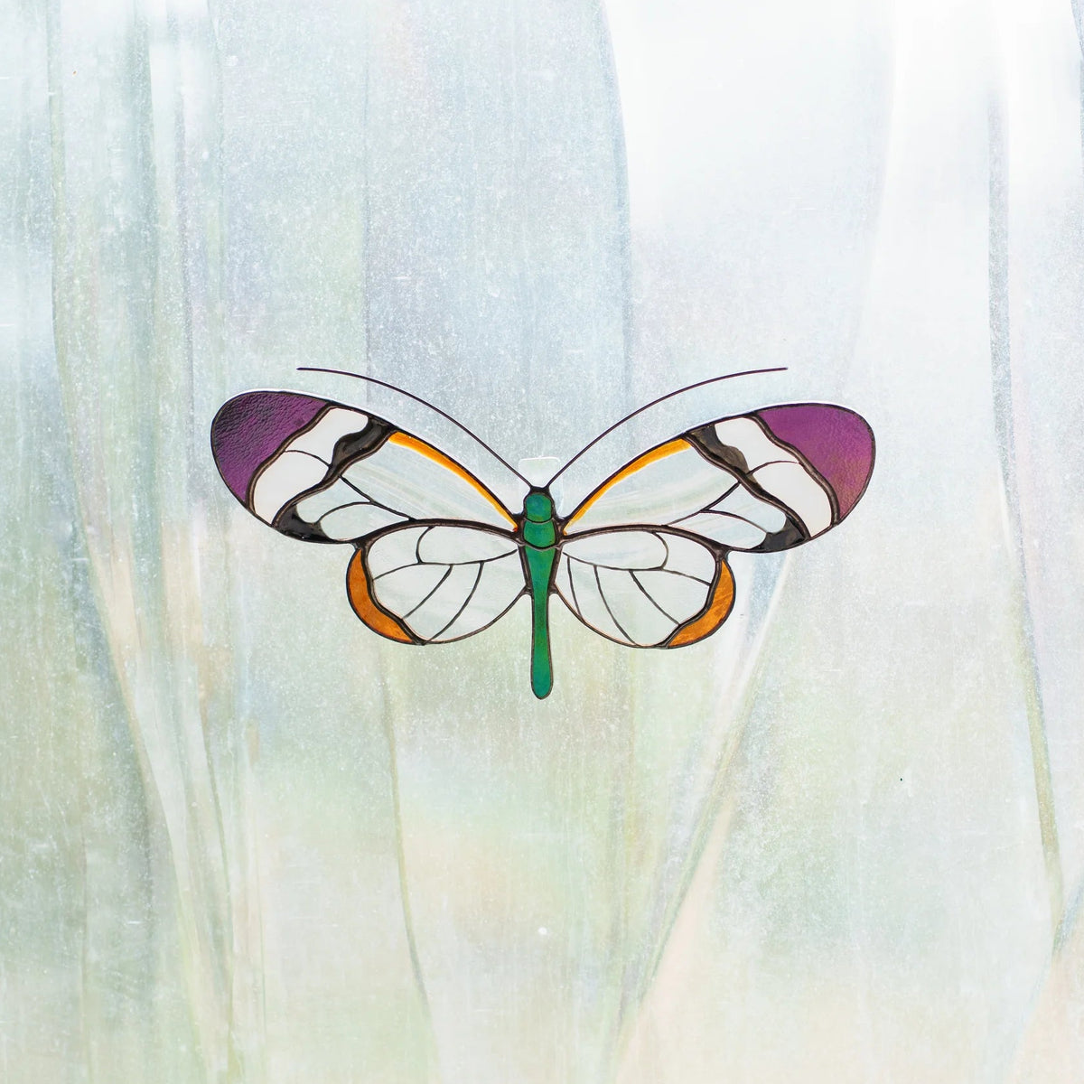 Glasswing butterfly stained glass suncatcher on a frosted window, purple and orange glass lit by daylight