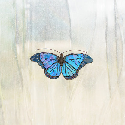 Blue morpho stained glass suncatcher on a window, iridescent blue and violet glass lit by the sun