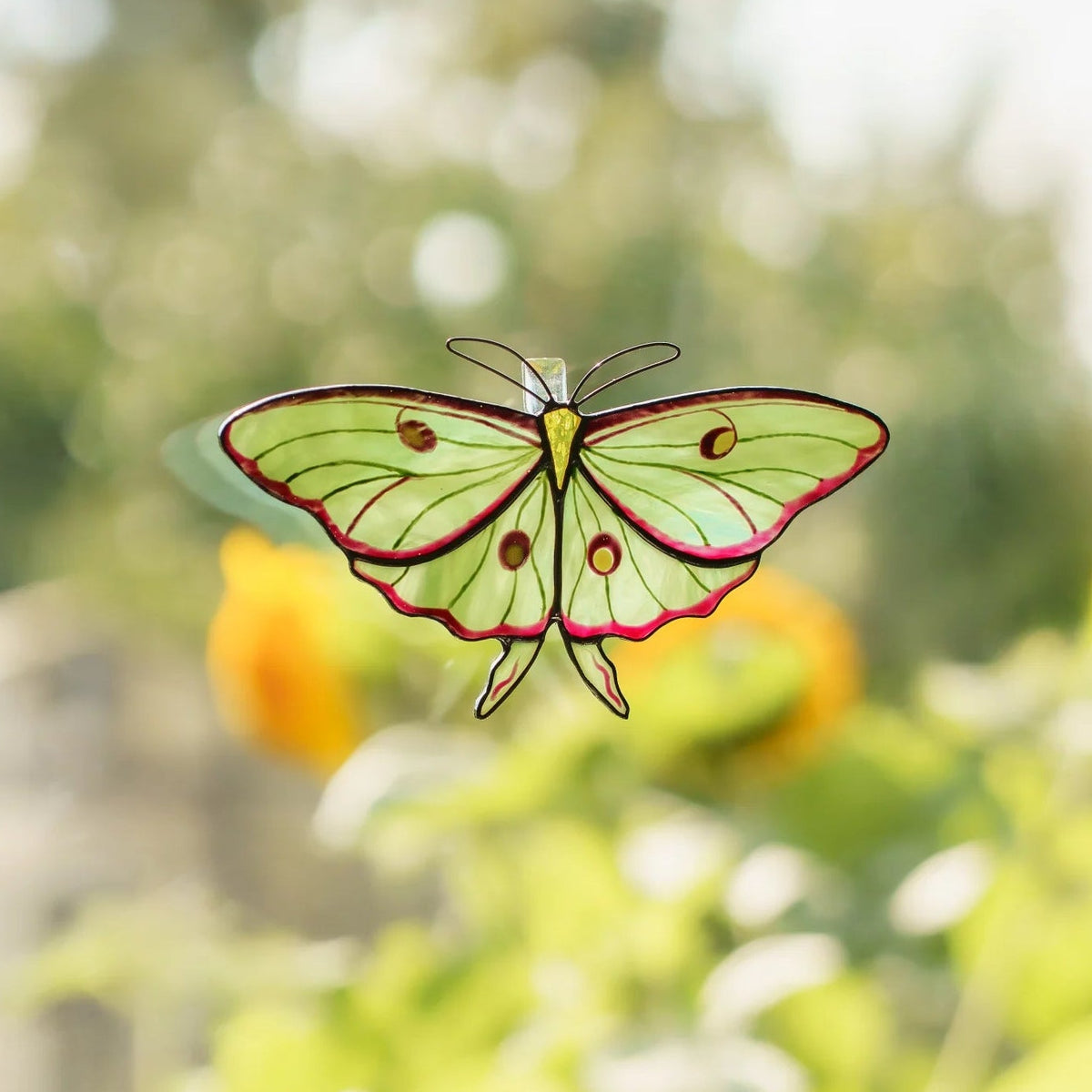Luna moth suncatcher on a window overlooking a sunny garden with sunflowers in the background