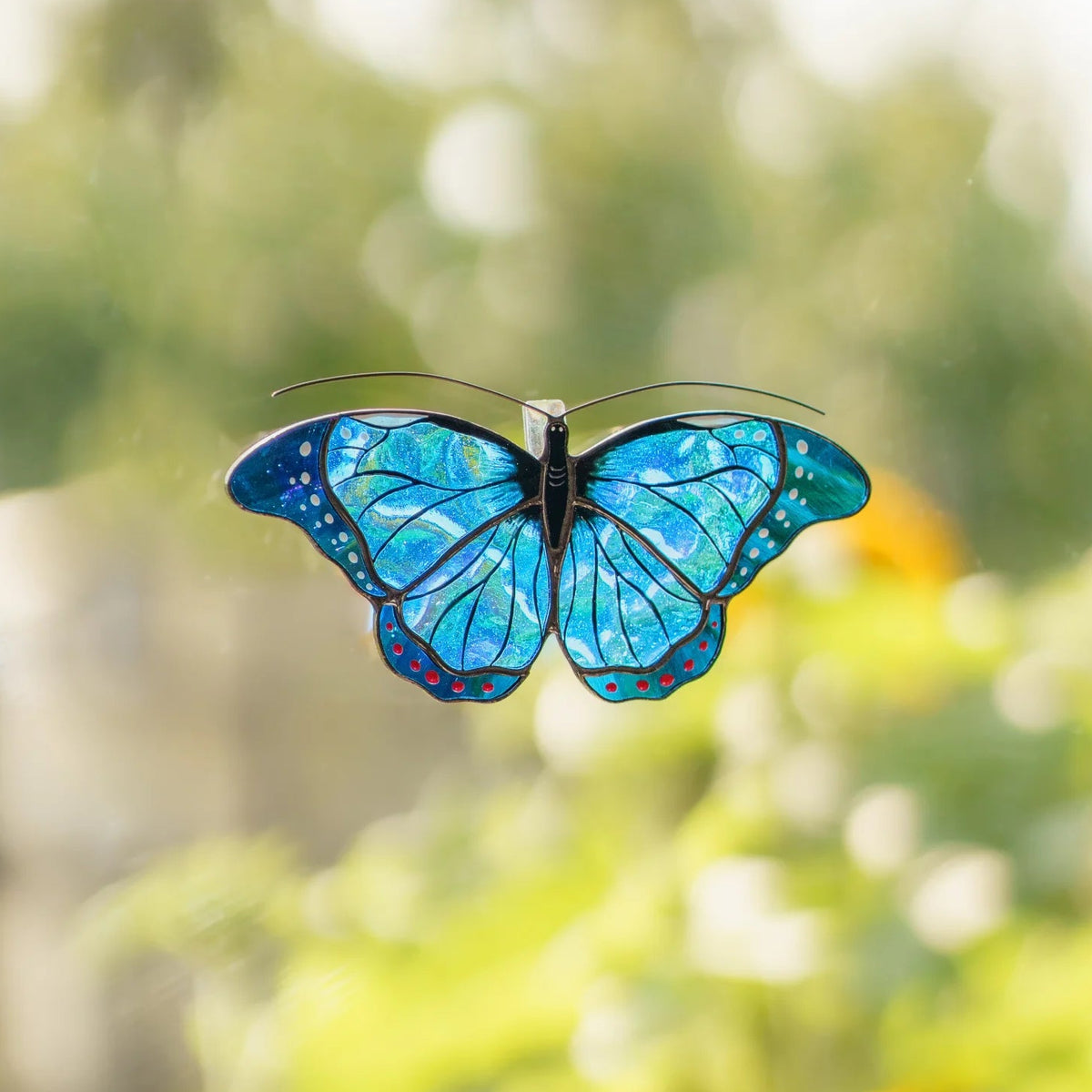 Blue morpho stained glass suncatcher on a garden window, shimmering blue glass against green leaves