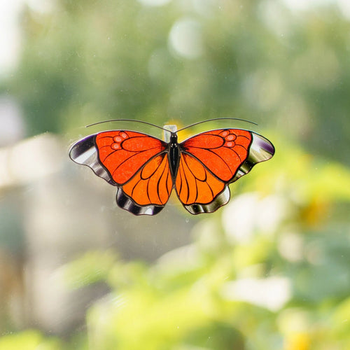 Orange stained glass butterfly suncatcher on a garden window, clear glass wing edges catching the sunlight