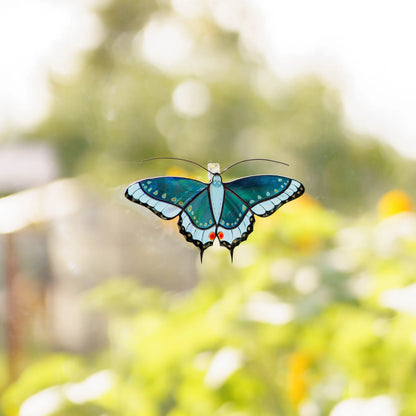 Blue swallowtail suncatcher on a garden window, teal glass and pointed tails glowing in the sun