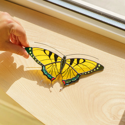 Yellow swallowtail suncatcher on a wooden windowsill, textured yellow glass casting golden light below