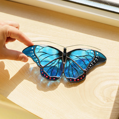 Blue morpho stained glass suncatcher on a wooden sill, iridescent glass scattering blue light in the sun