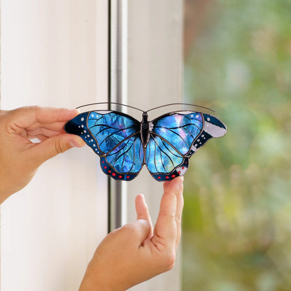 Blue morpho suncatcher held at a window frame, iridescent blue glass catching the daylight
