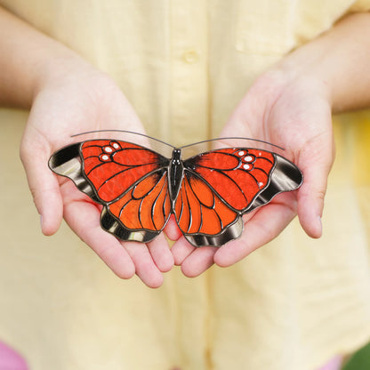 Red-orange stained glass butterfly suncatcher with clear wing edges resting in cupped hands